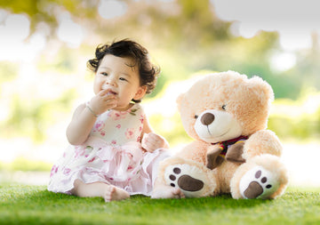baby girl laughing with her teddy bear next to her