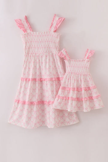 Pink tiered dress with smocked bodice and charming bow detail, perfect for matching outfits.