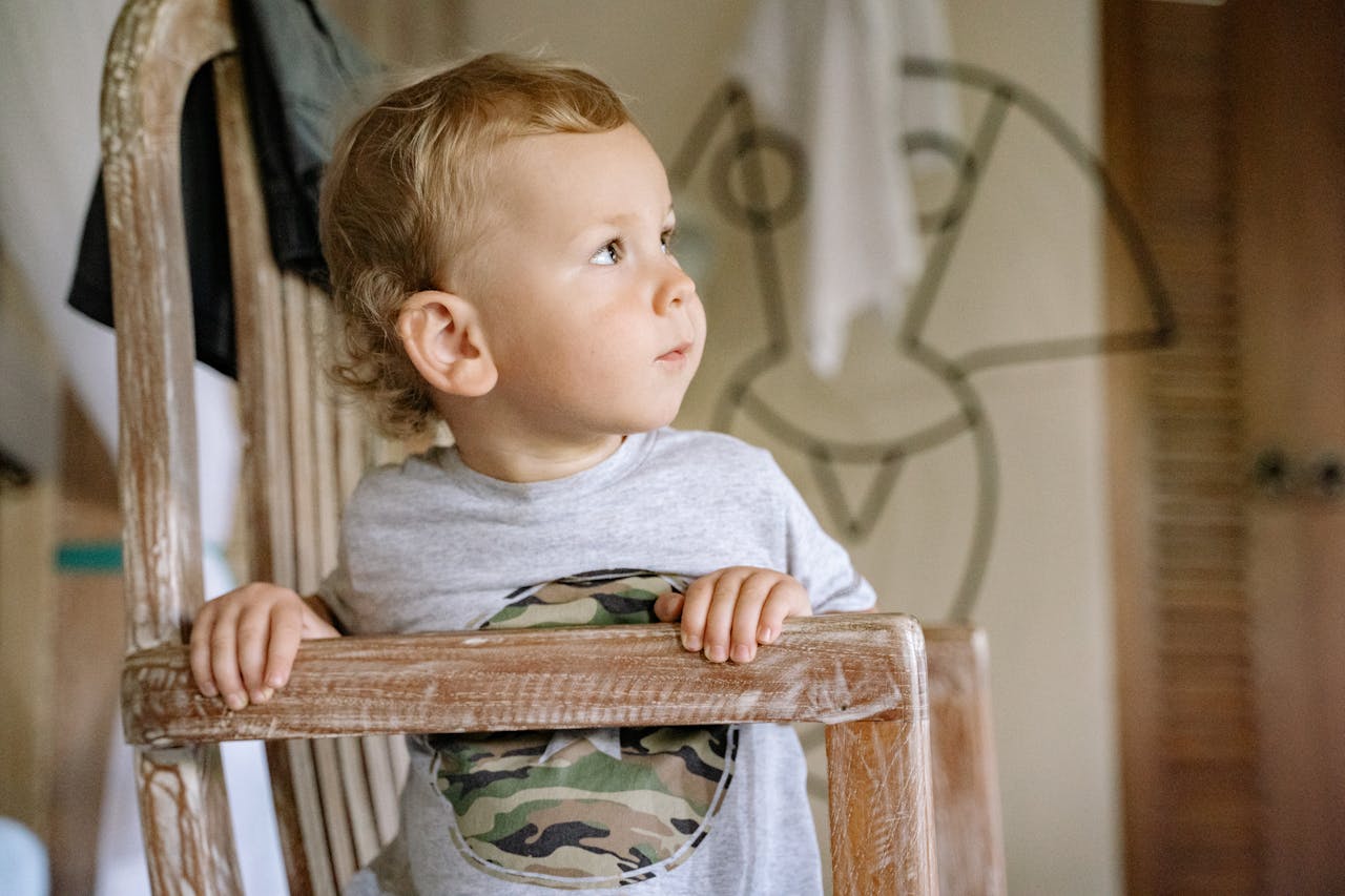 child in gray longs sleeve shirt sitting on brown wooden chair