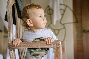 child in gray longs sleeve shirt sitting on brown wooden chair