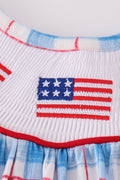 A charming smocked dress with colorful flag embroidery, perfect for festive occasions.