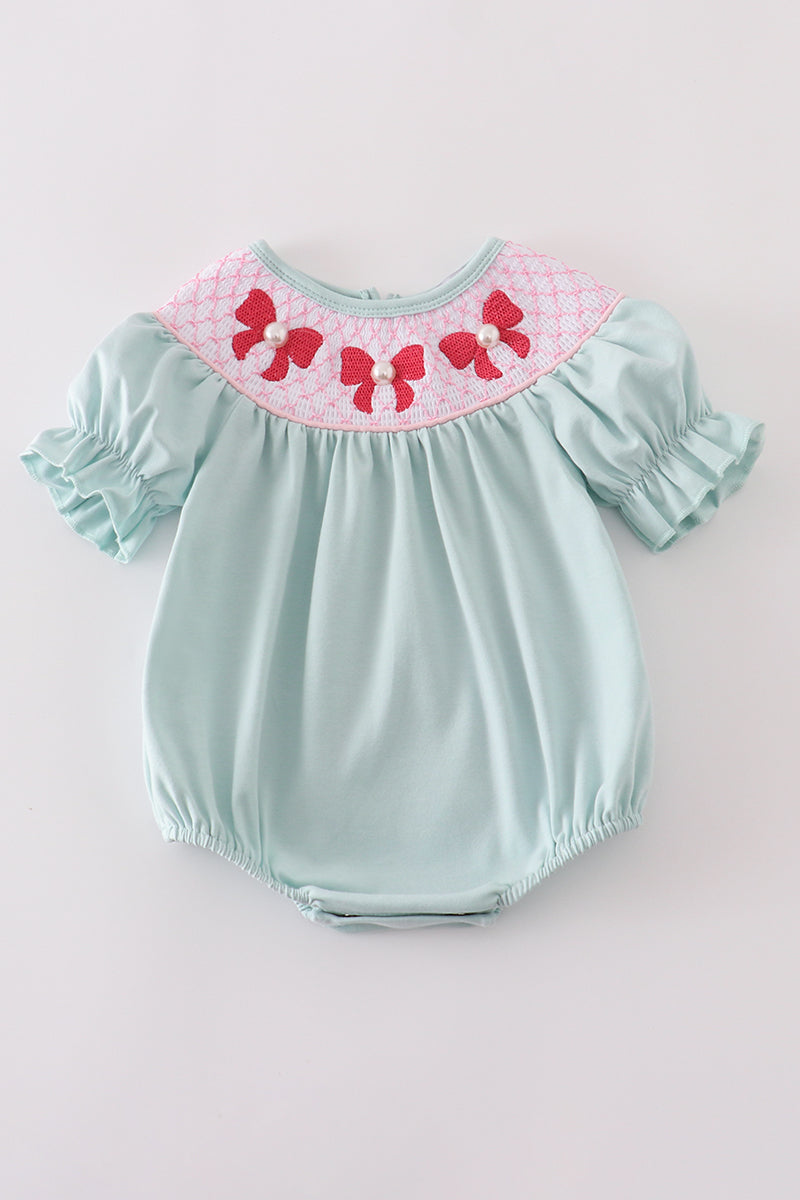 A charming blue bubble romper with pearl smocking and a cute bow accent.