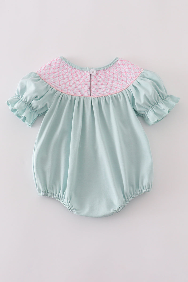 A charming blue bubble romper with pearl smocking and a cute bow accent.