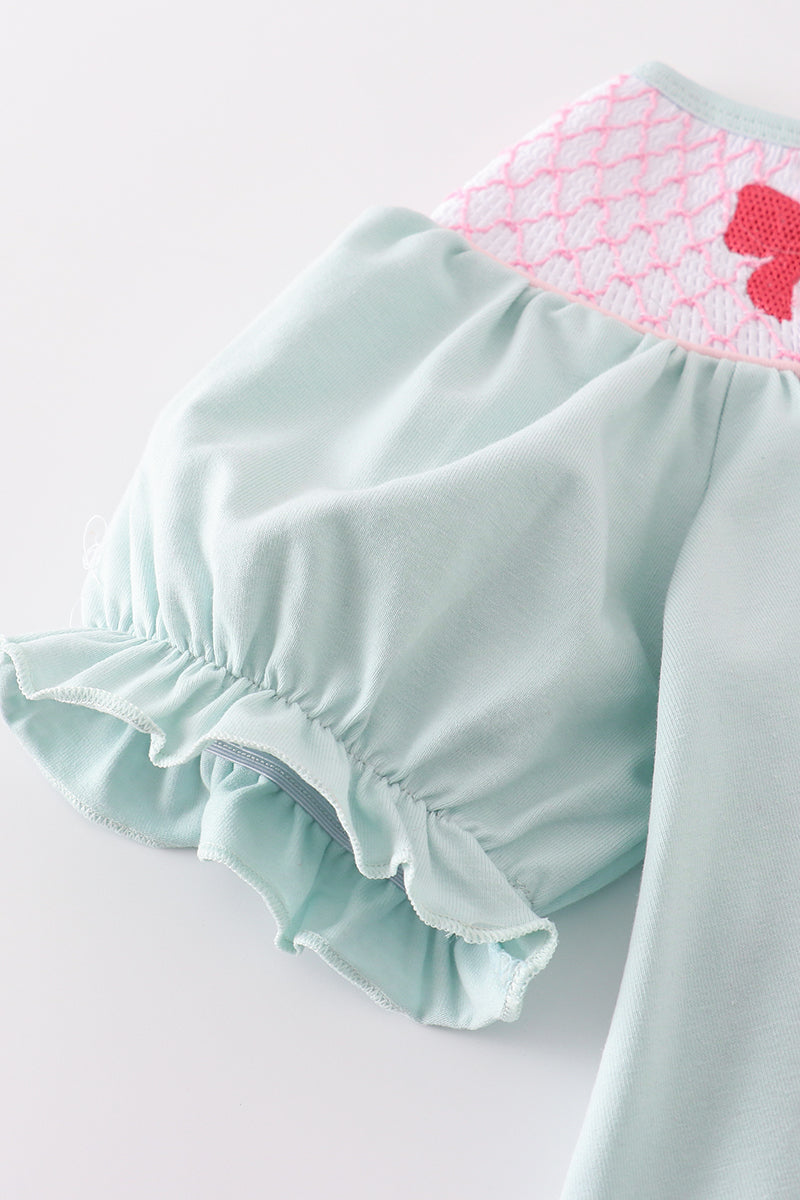 A charming blue bubble romper with pearl smocking and a cute bow accent.