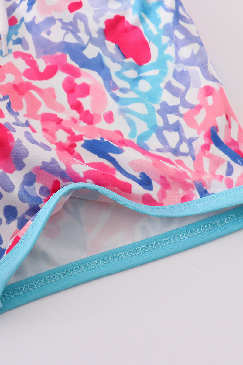 Bright swim trunks with vibrant tropical sunset and ocean wave patterns for kids.